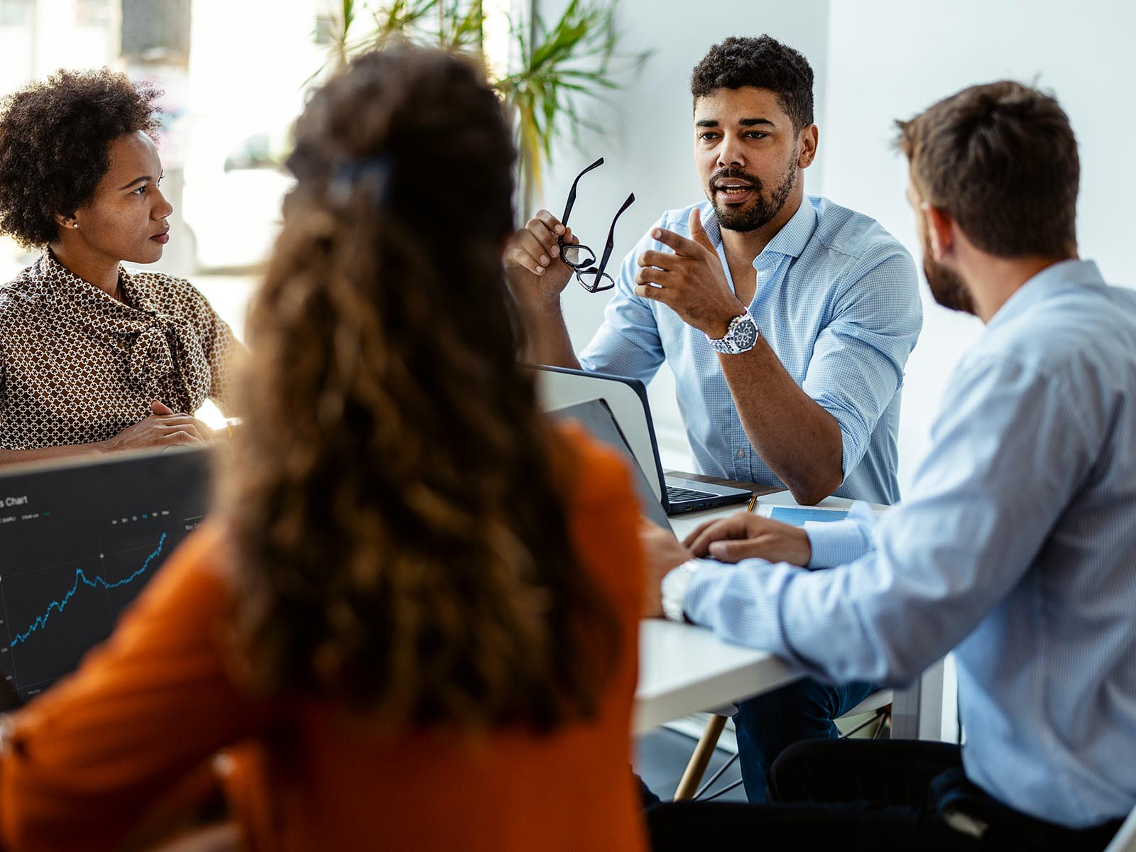 A group of colleagues sat around a table with their computers having a deep discussion