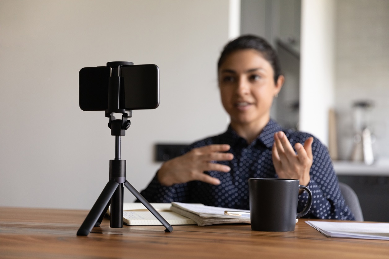 Millennial Indian female vlogger or coach recording or video live broadcast on smartphone at home