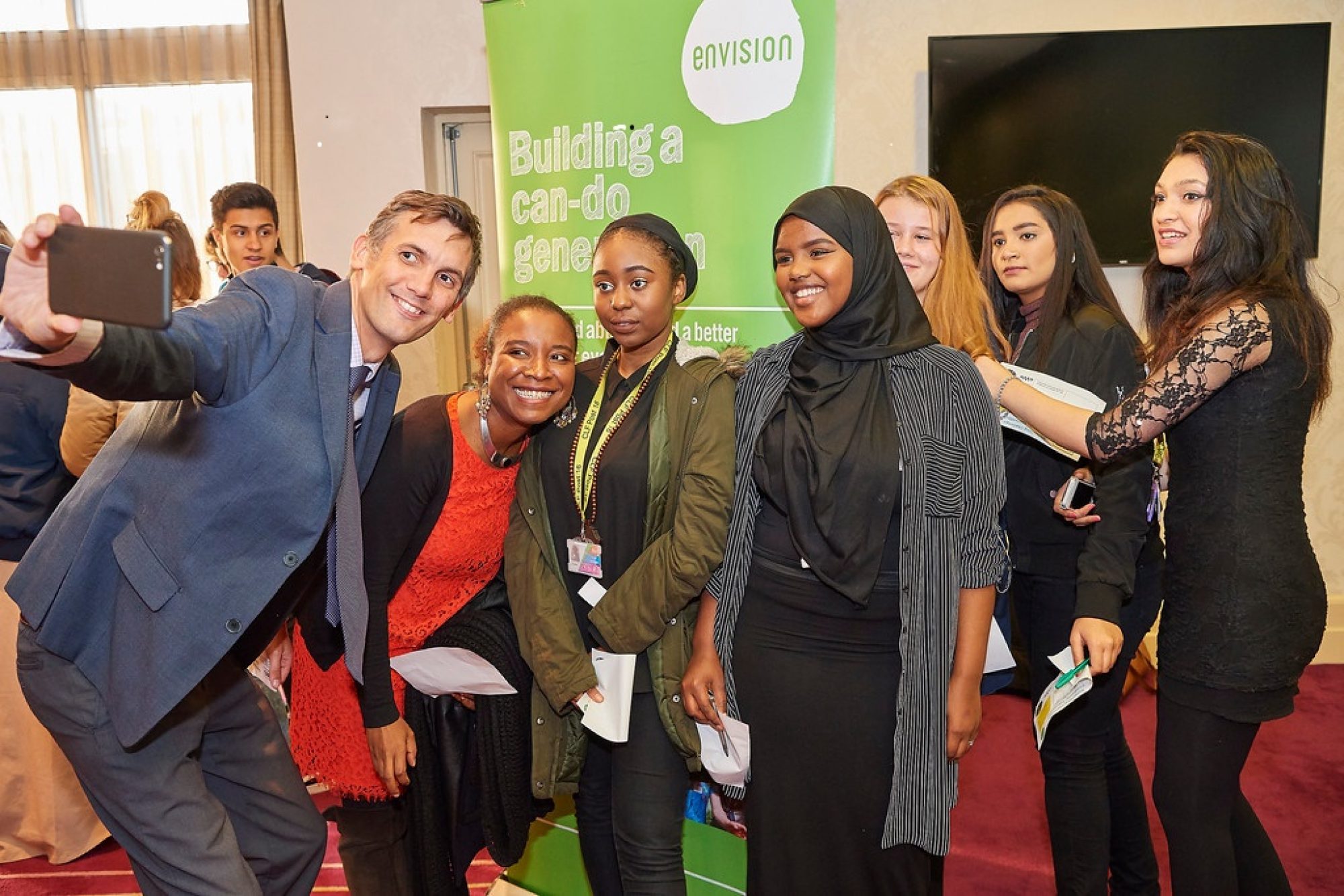 A diverse group of young woman taking a selfie with a gentleman in a suit at the Envision event