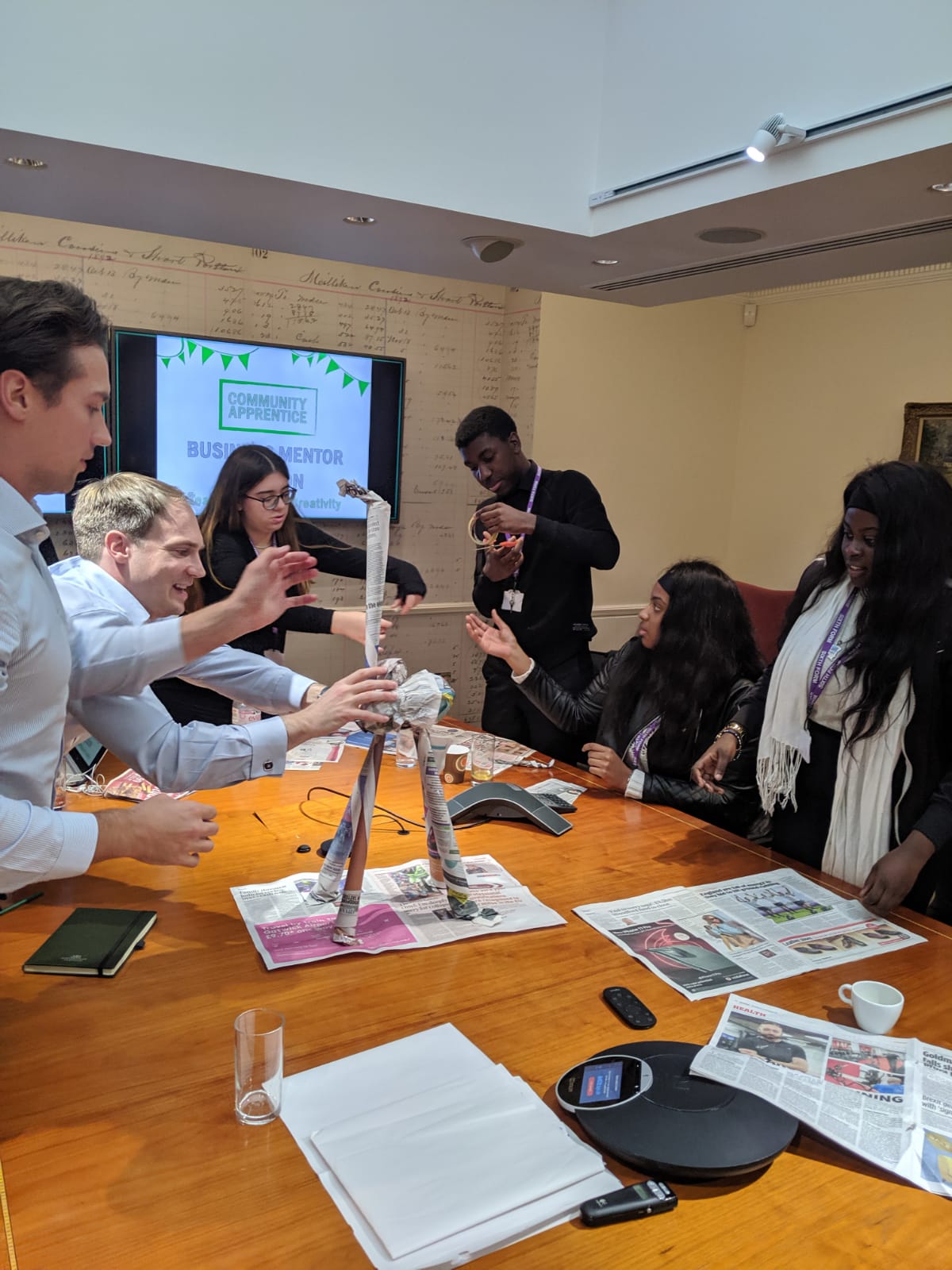 A diverse group of young people using their teamwork skills to create a sculpture out of newspaper.